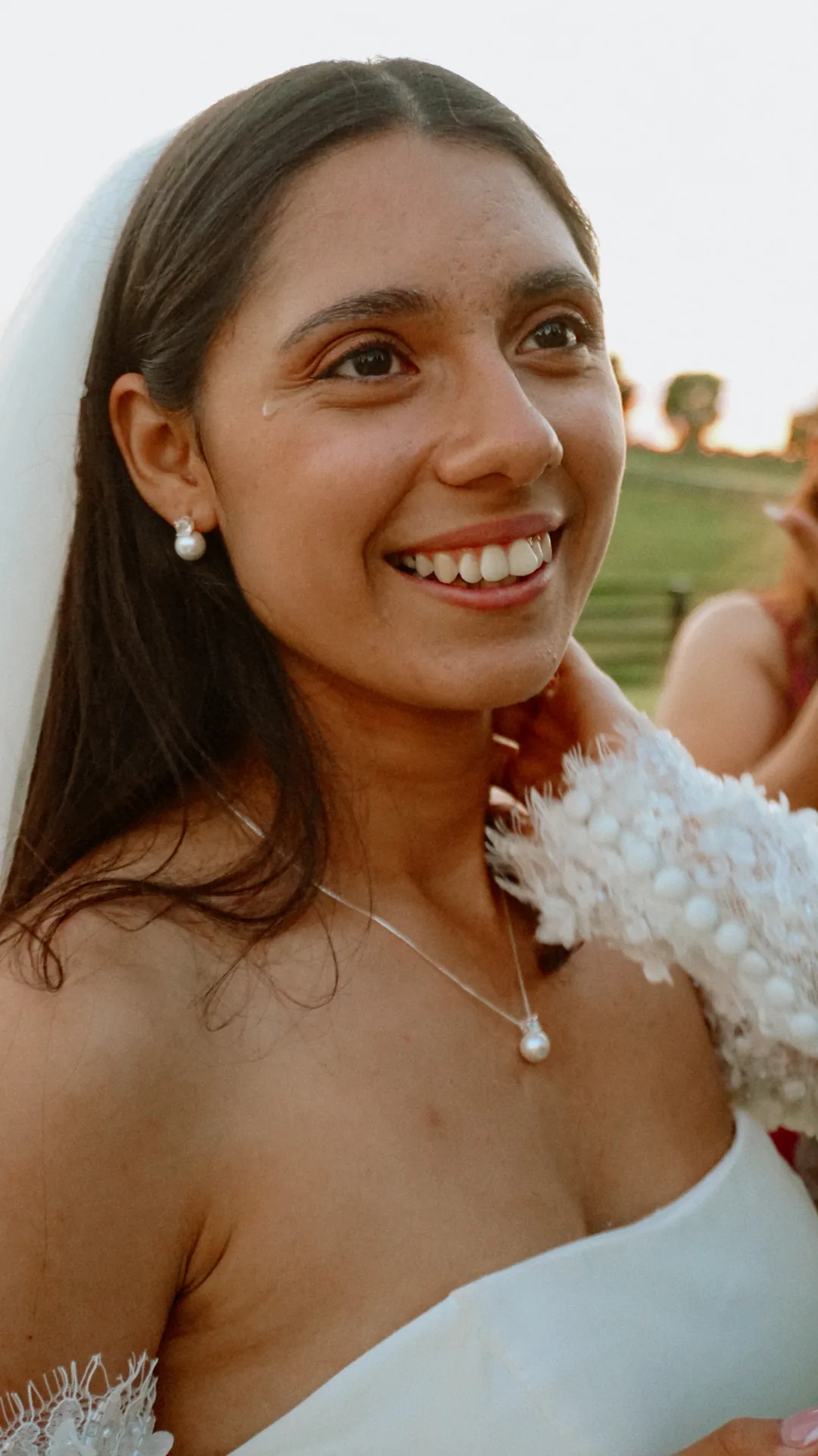The bride smiling with a tear on her cheek, pearl earrings catching the light