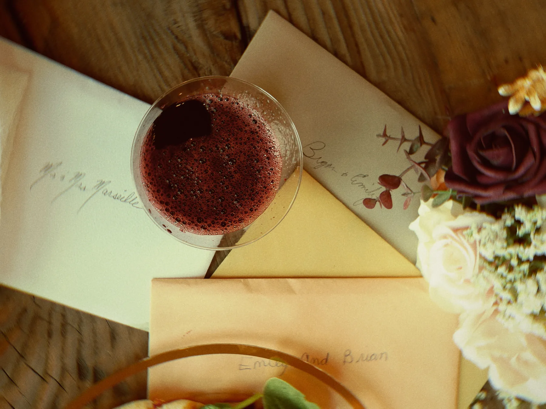 A cocktail, handwritten envelopes and roses on a wooden table