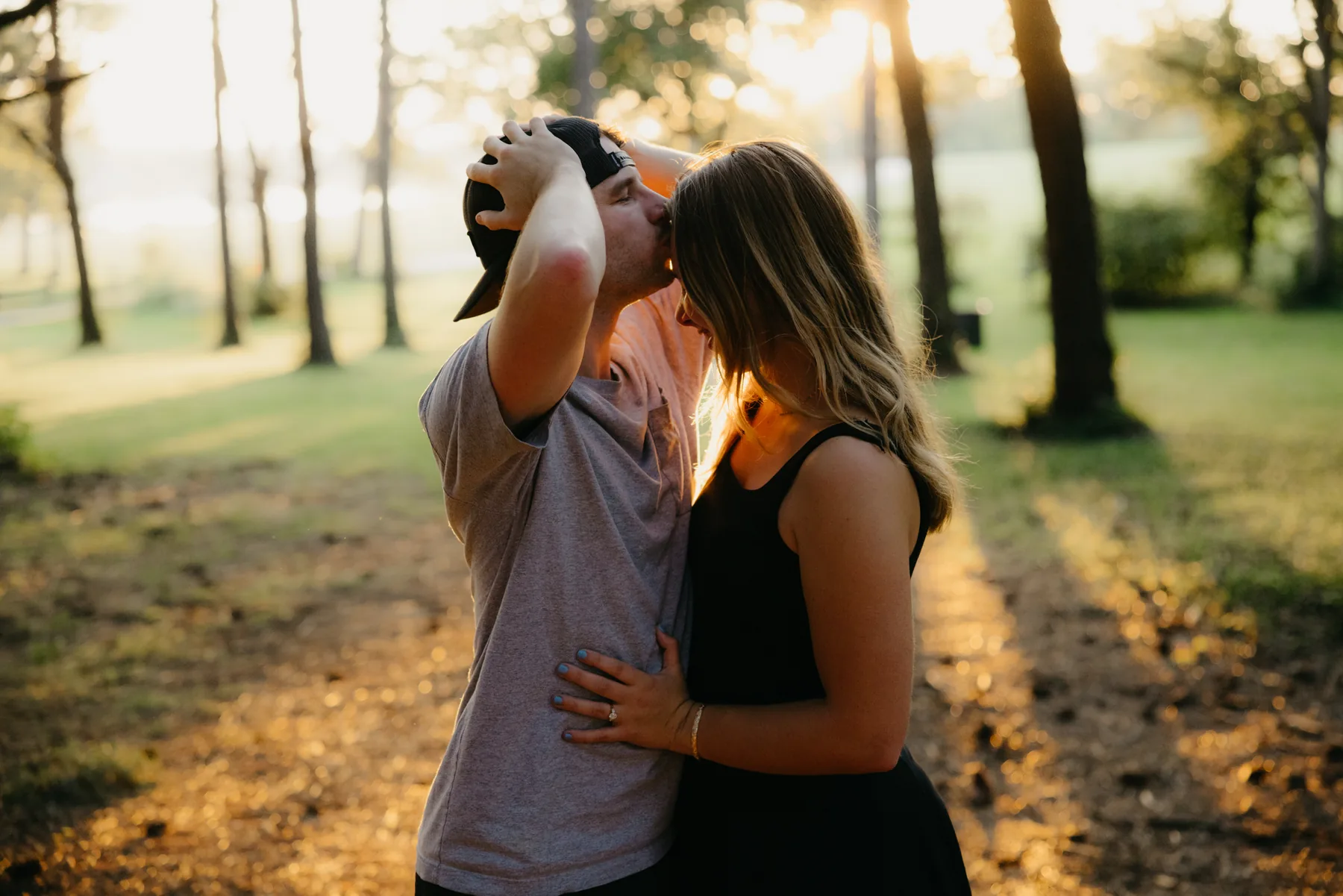 A forehead kiss in a green field with the sun low behind the trees