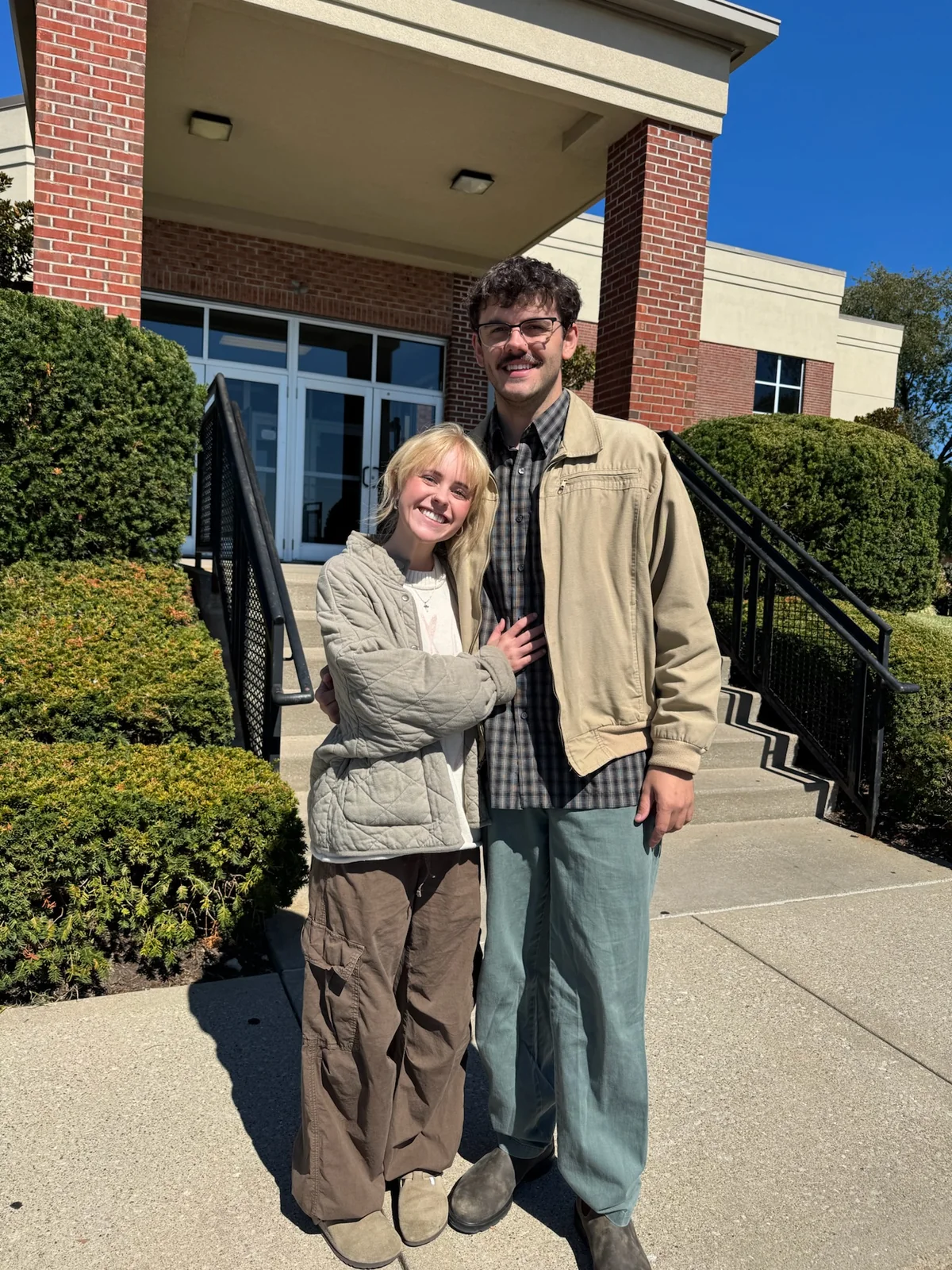 Nathaniel and Clara standing together in the sun outside a brick building