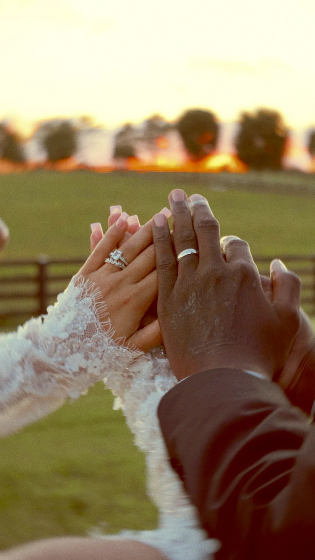 Their hands and new rings held up against a black fence and the sunset