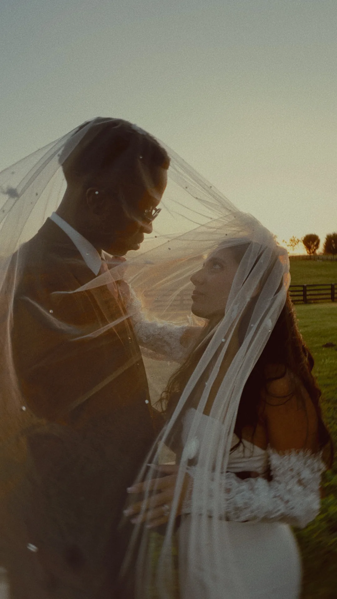 Under the veil, her looking up at him, the fence line and the last light behind them